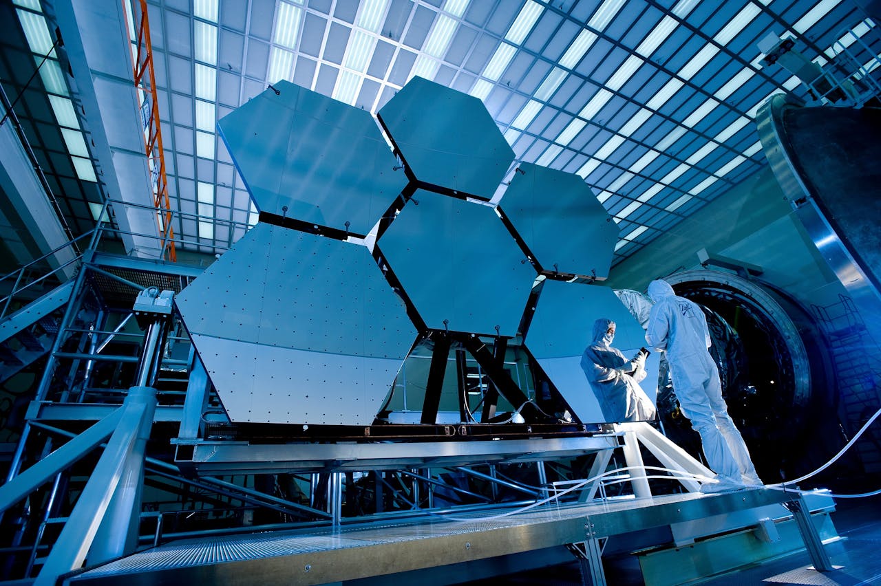 Services Engineers in protective suits work on telescopic mirrors in a high-tech lab.